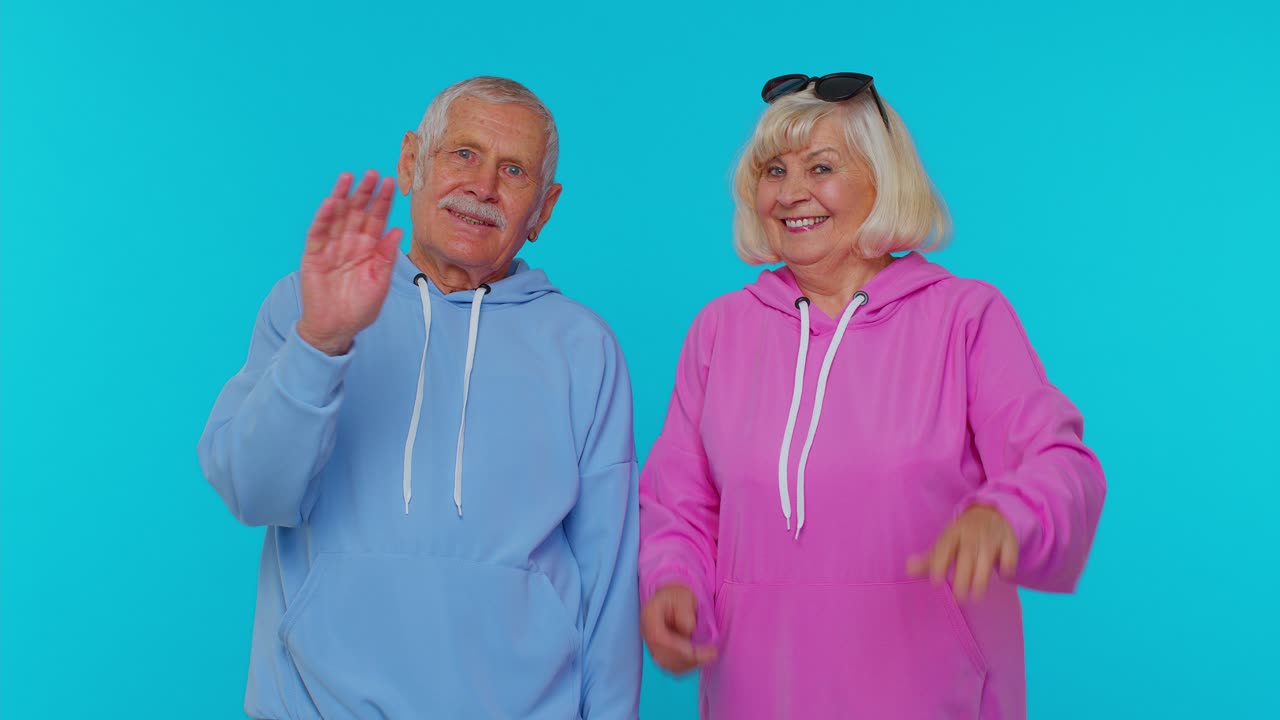 Elderly granny with grandfather smiling friendly at camera, waving hands gesturing hello or goodbye