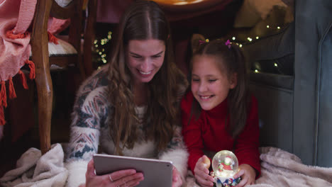 Caucasian-mother-and-daughter-waving-while-having-a-video-chat-on-digital-tablet-under-blanket-fort-