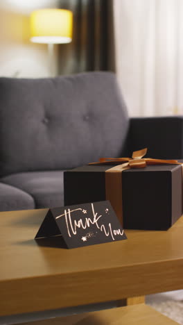 vertical video of present in gift wrapped box decorated with ribbon with thank you card on table in lounge