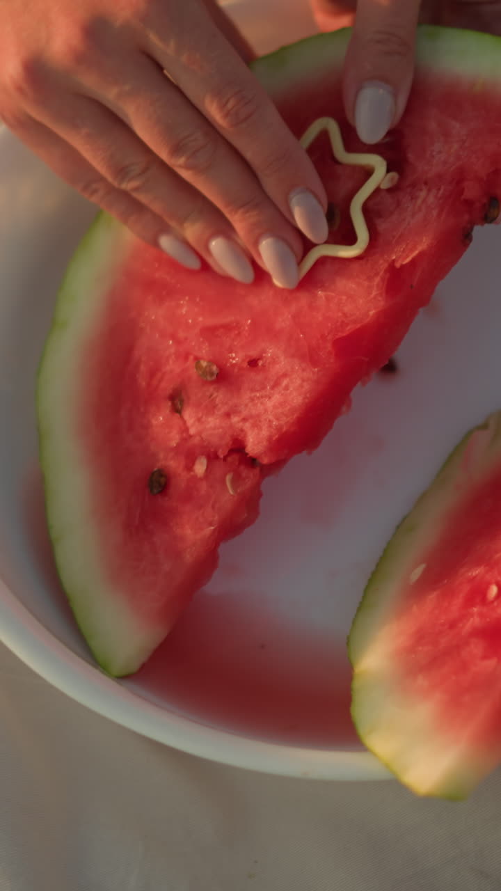 primer plano de la mano presionando un cortador en forma de estrella en una rebanada de sandía fresca y jugosa en un plato blanco, la corteza verde y la carne roja vibrante contrastan hermosamente