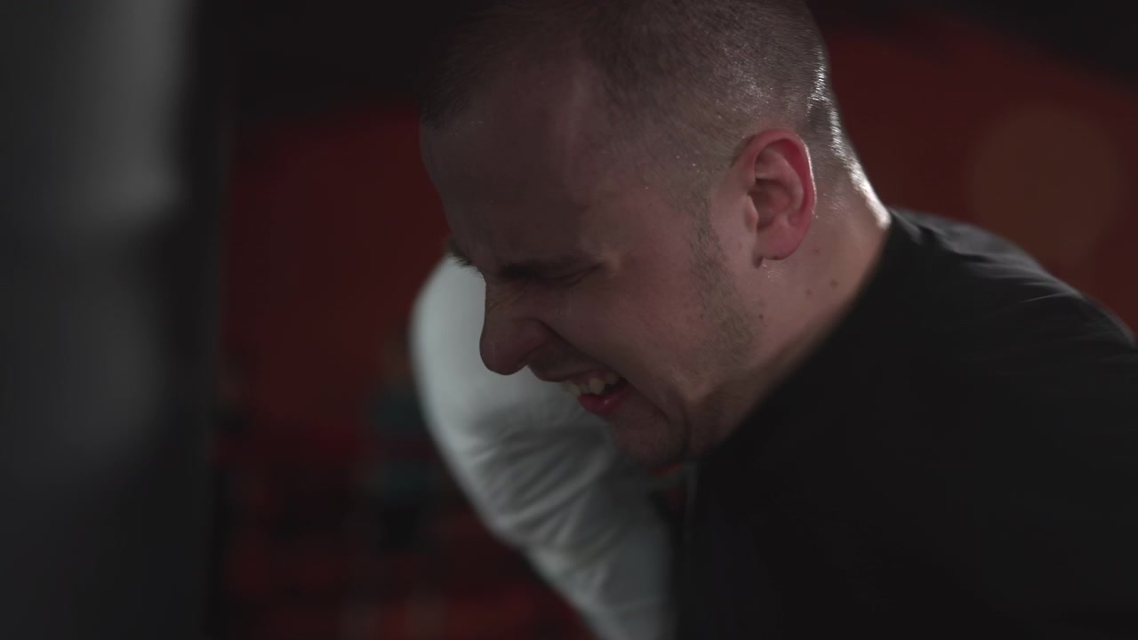 Adult man with shaved hair trains boxing in close side view, white glove near mouth and chin, tense expression, blurred combat studio background, low dramatic light, strong contrast, intense