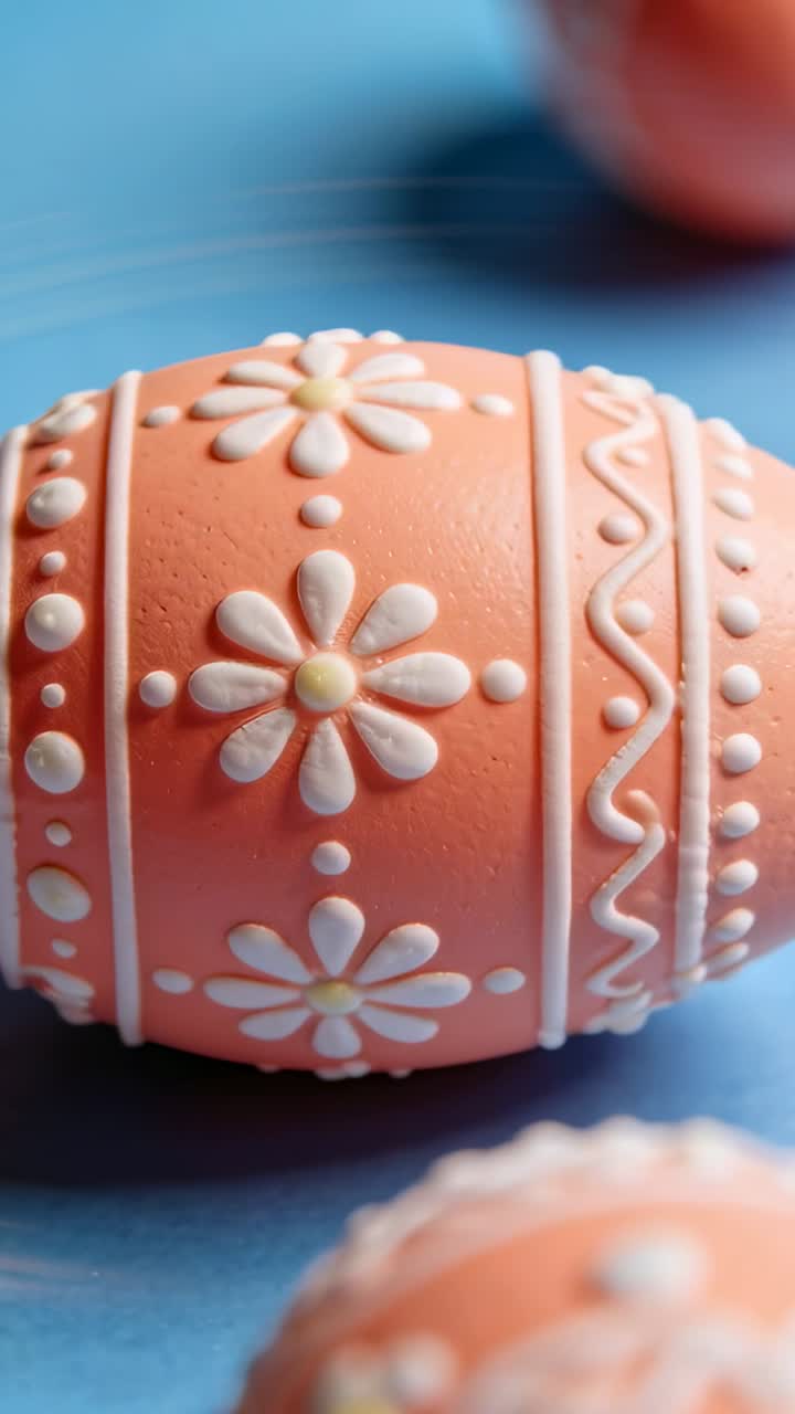 Vertical video: Panning camera revealing peach decorated egg on blue table, showing piped motifs