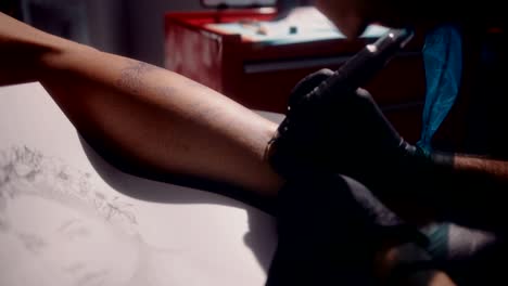 artista del tatuaje usando equipo de tatuaje y dibujando en la pierna del cliente