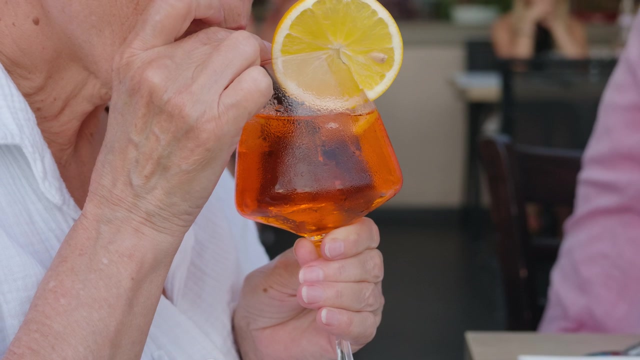 Primo piano della mano di una donna anziana che tiene un cocktail spritz all'arancia.
