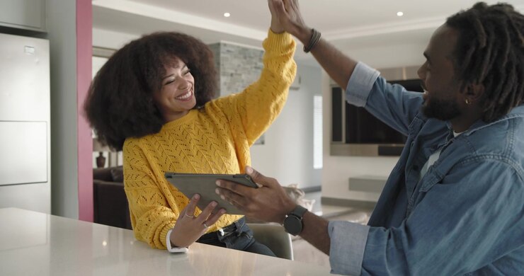 African American couple in kitchen, woman tapping tablet after man leaning in, reacting to screen