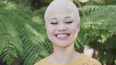 retrato de una feliz mujer biracial en el jardín con grandes hojas verdes en cámara lenta