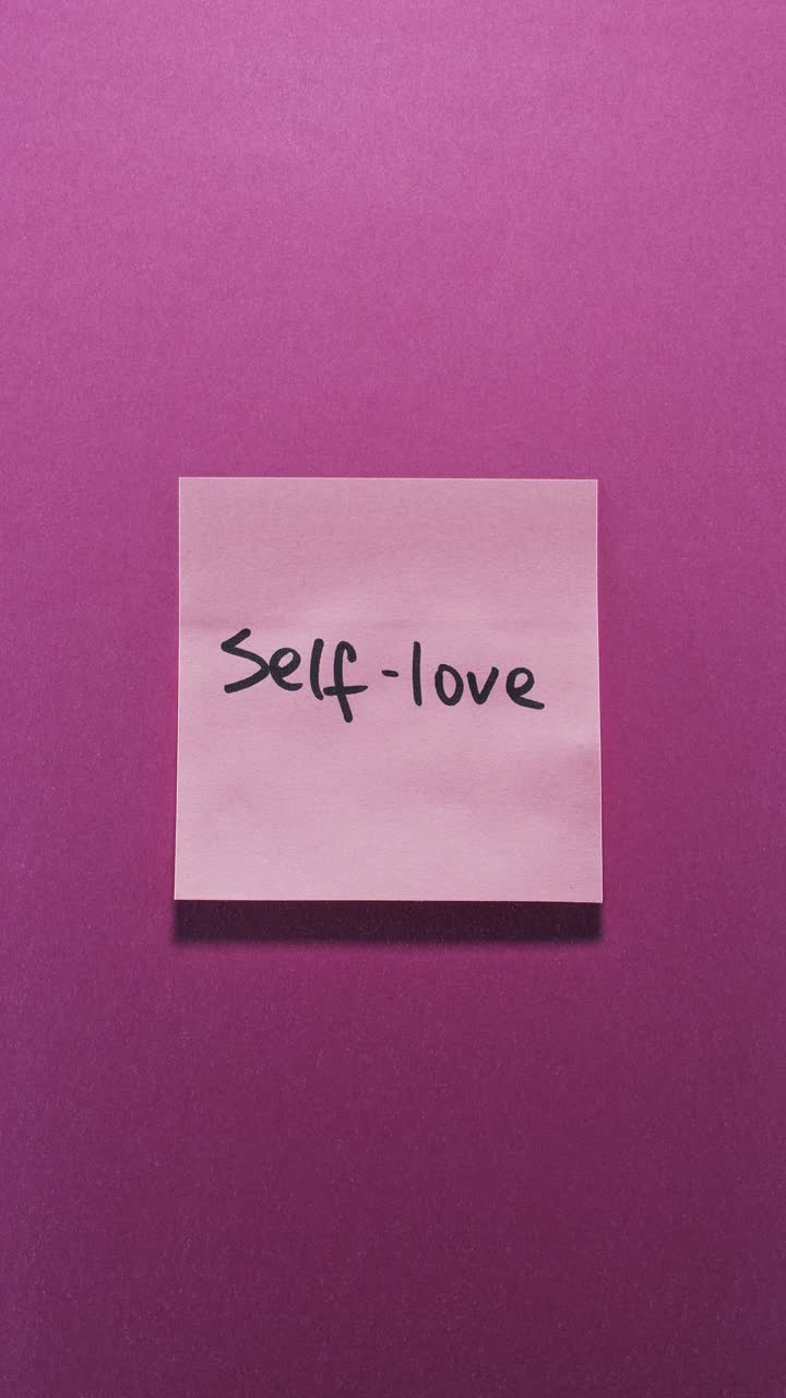 Hands posting Self-love sticky note on pink wall, expressing self care