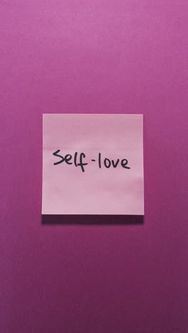 hands posting self-love sticky note on pink wall, expressing self care