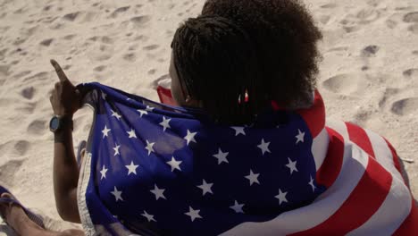 Couple-wrapped-in-American-flag-sitting-together-on-the-beach-4k