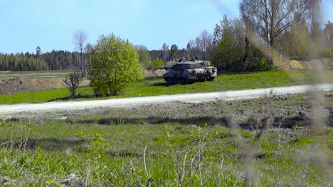 gorgeous footage of a british army military challenger 2 4034 tank hidden behind some bushes in a grassy green field and aiming at a tree line in the back with its large cannon during sunny warm day.