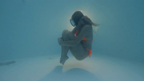 Pretty-Girl-in-Swimsuit-Floating-Curled-Up-Underwater-with-Vintage-Diving-Goggles