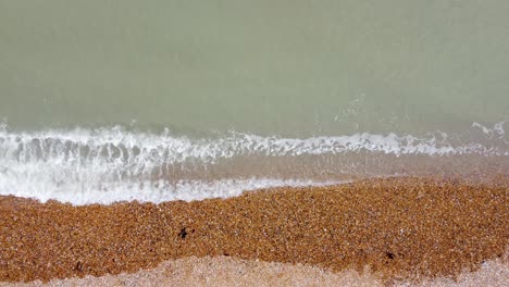 Simple-drone-footage-of-waved-lapping-over-a-pebbled-beach-in-Deal,-Kent