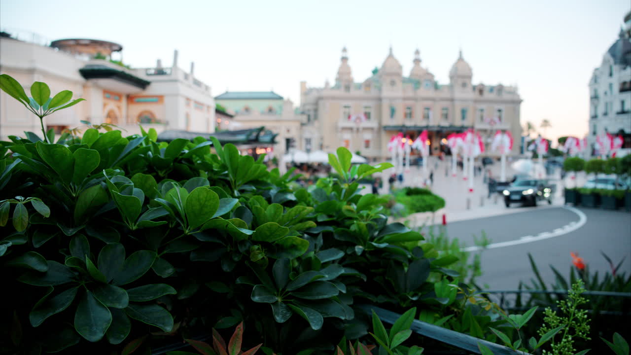 Distant, blurry street view of multiple Monegasque flags waving in front of the Monte Carlo Casino