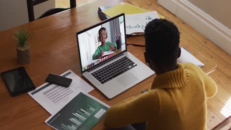 maestra afroamericana hablando y tomando notas mientras tiene una videollamada en una computadora portátil en casa