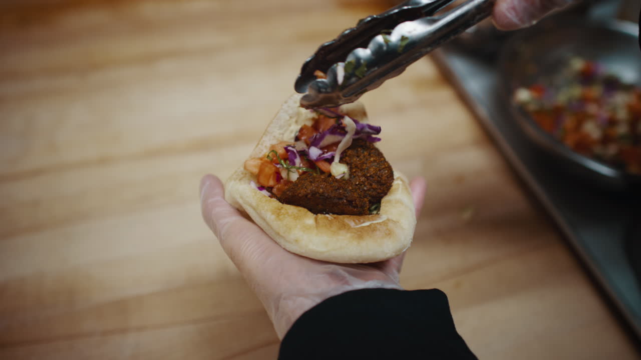 Chef che inserisce cipolle all'interno di un falafel nel pane pita.