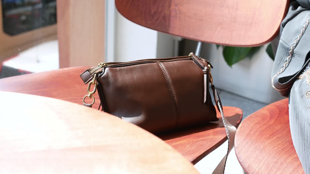 Brown Leather Crossbody Bag on Wooden Chair in a Cafe