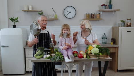 Fröhliches-Veganes-Seniorenpaar-Tanzt-Mit-Enkelin,-Während-Es-In-Der-Küche-Gemüse-Kocht