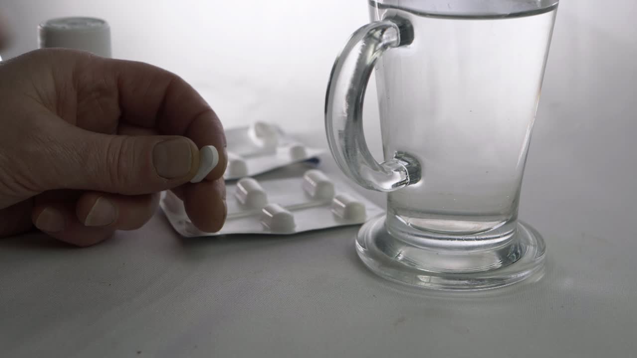 Hands taking headache tablets with glass of water close up shot