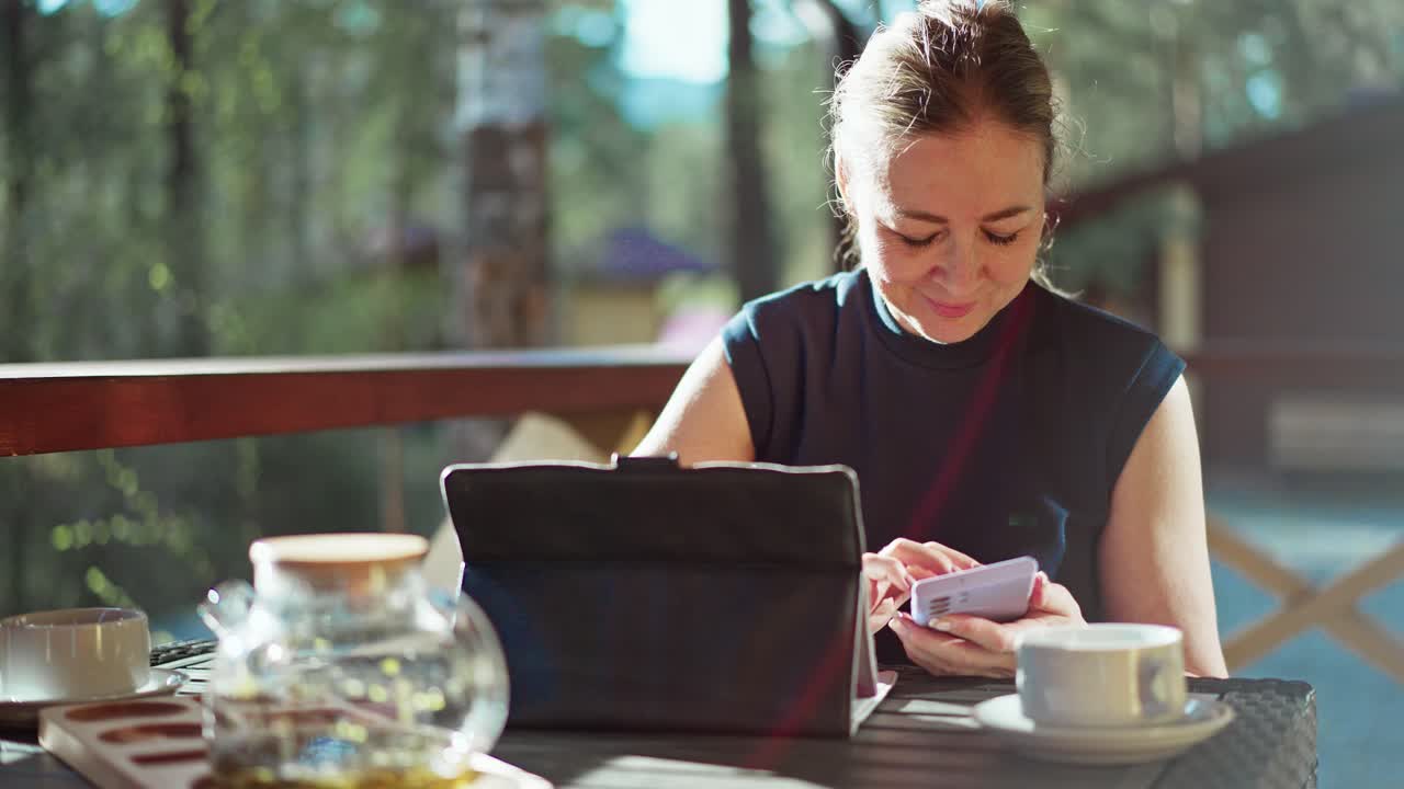 Woman working outdoors on tablet and phone at a cafe