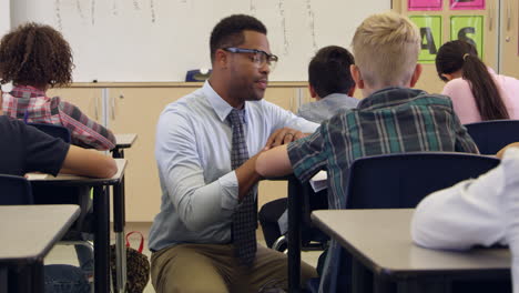 teacher kneeling down to help a boy at his desk, shot on r3d