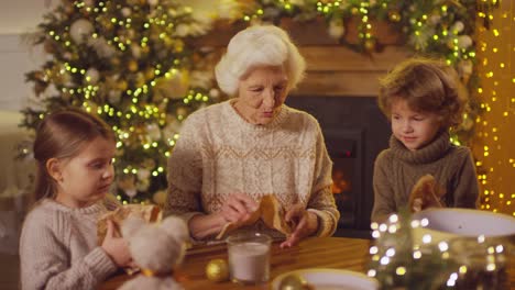 abuela con dos nietos sentados en la mesa envolviendo regalos en una habitación con adornos navideños