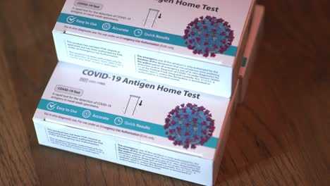 covid 19 at home antigen test kit for coronavirus 3 white and blue boxes of tests stacked up wide shot focusing on top and bottom boxes and slowly panning around table