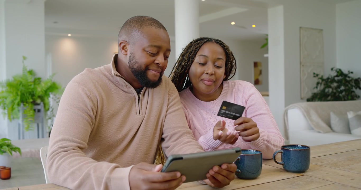Couple africain assis à table, l'homme tapotant sur une tablette pendant que la femme montre une carte, confirmant le paiement