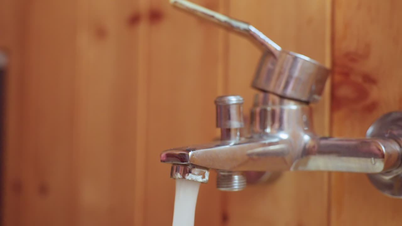 close up of person hand turning off sauna bathroom chrome tap, water flow slowing to gentle drip against wood panel background, fingernail and metal detail