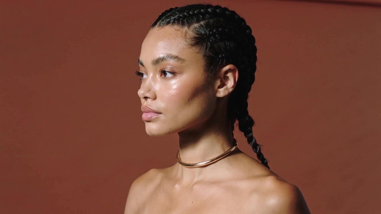Trägerloses Model posiert auf Kommando, macht subtile Kopf- und Augenanpassungen im Studio mit goldenem Halsband.