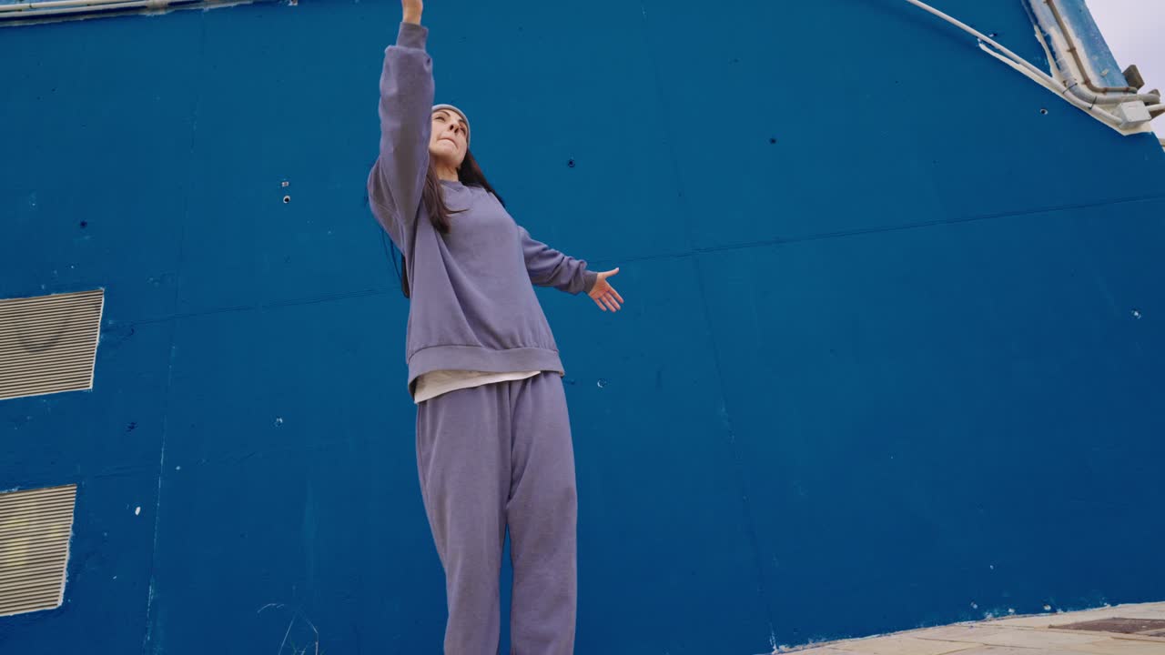 Woman in Sweatsuit Dancing Against Blue Wall