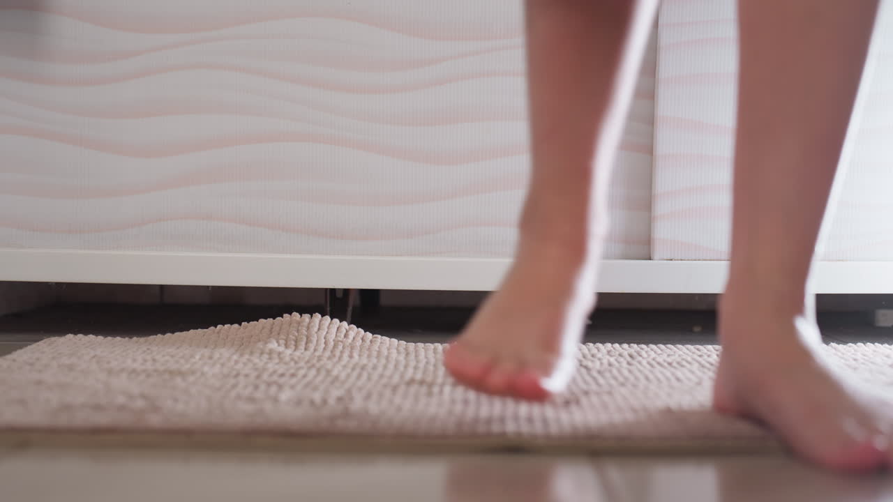 Low view shows soft pink bath mat on tiled floor, woman legs step from tub onto rug, water dripping as she exits, hygiene and comfort moment, anti slip absorbent texture highlighted under panel