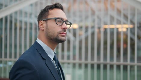 thoughtful 30-year-old french businessman in glasses walking in the city by office building - close up tracking shot