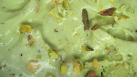 sharp macro focus on a green pistachio ice cream scoop with raw nut details scattered around