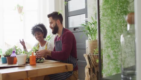 Video-of-happy-diverse-couple-tending-to-plants-at-home,-with-copy-space