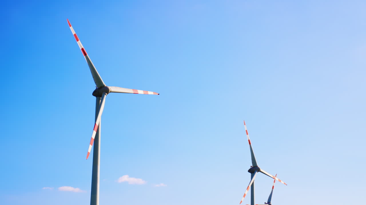 Tall wind turbines under blue. Two large wind turbines rotate against a clear blue sky, showcasing renewable energy and sustainability efforts