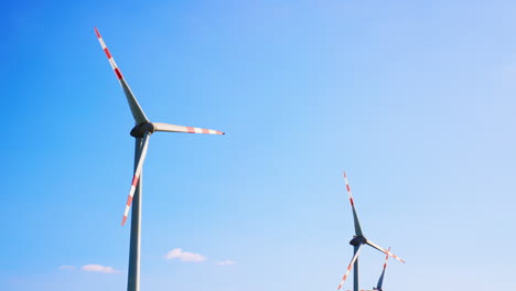 tall wind turbines under blue. two large wind turbines rotate against a clear blue sky, showcasing renewable energy and sustainability efforts