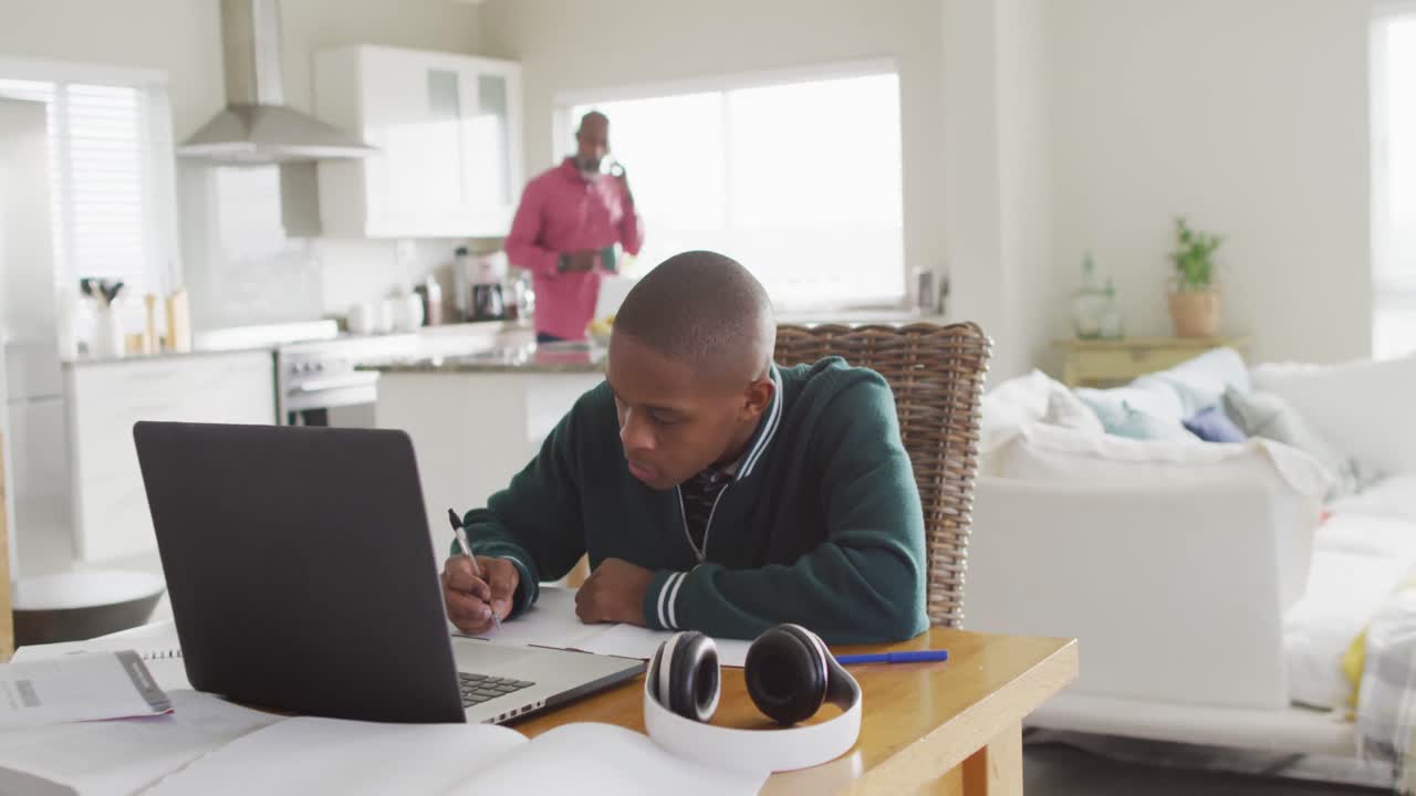 Video of focused african american boy with laptop having online lessons at home