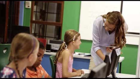 teacher assisting school kids on personal computer in classroom