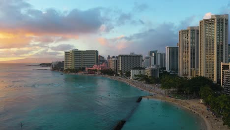 hawaiian beach surfers and tourists near beachfront resort hotel buildings swimming and relaxing in sand on waikiki beach in honolulu, hawaii at sunset
