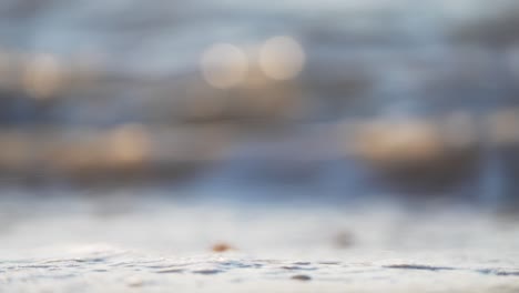 Low-static-close-up-shot-of-small-waves-breaking-on-the-beach,-with-the-sun-low-on-the-horizon,-tight-focus