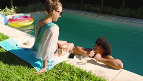 relaxing by pool, diverse couple enjoying drinks and sunshine on summer day