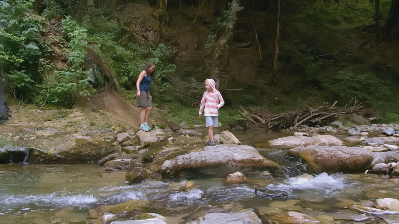 Ibu dan anak laki-laki mendaki di sepanjang aliran sungai pegunungan