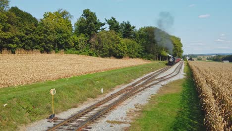 an antique restored locomotive and passenger coaches approaching on a sunny day traveling thru the countryside viewed from an elevated height