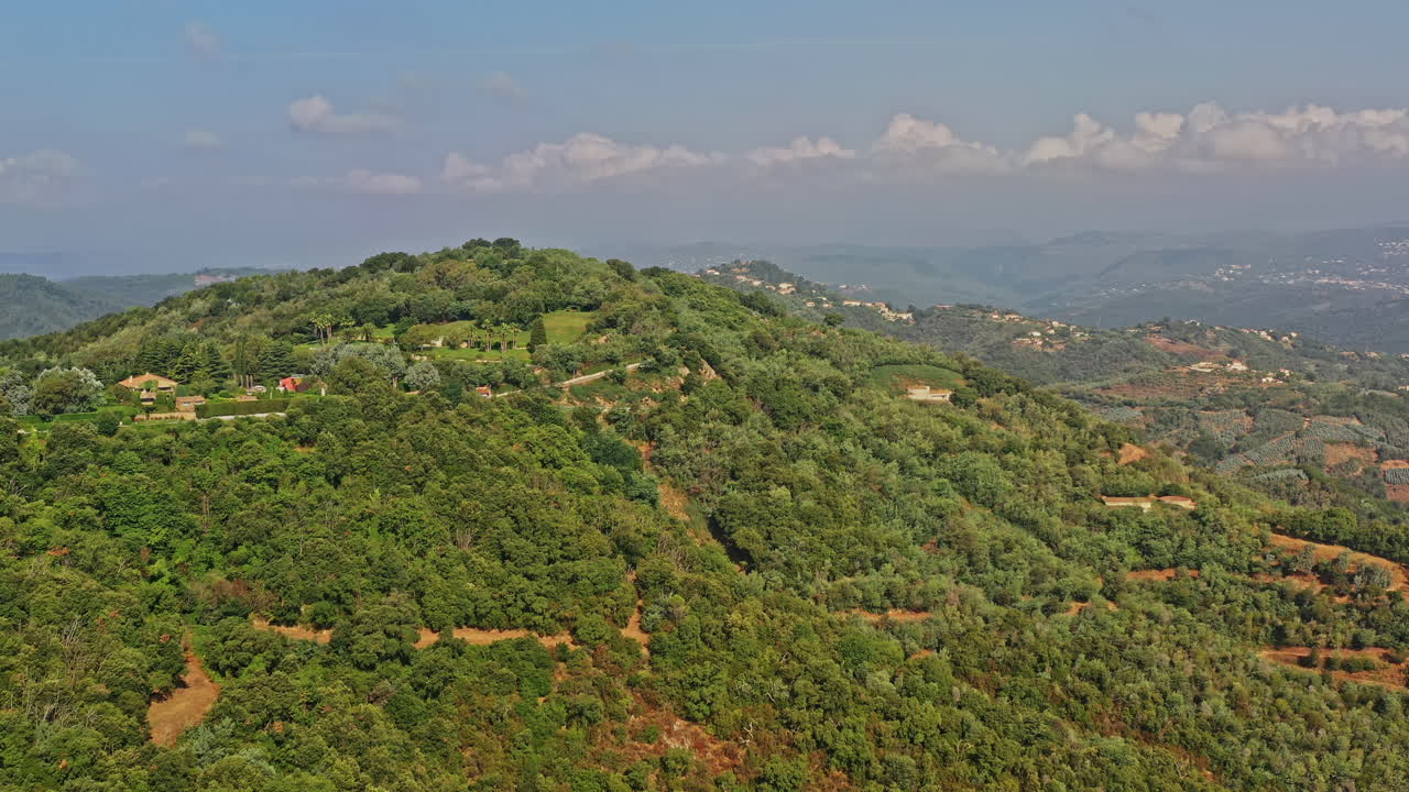 tanneron francia antena v17 que establece una toma impresionante, el vuelo de drones sobre una colina revela un pueblo al pie de la colina, valles verdes y plantaciones rurales en un tranquilo día soleado - julio de 2021