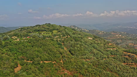 Tanneron-France-Aerial-v17-establishing-breathtaking-shot,-drone-flyover-a-hill-reveals-foothill-village,-green-valleys-and-rural-plantations-on-a-tranquil-sunny-day---July-2021