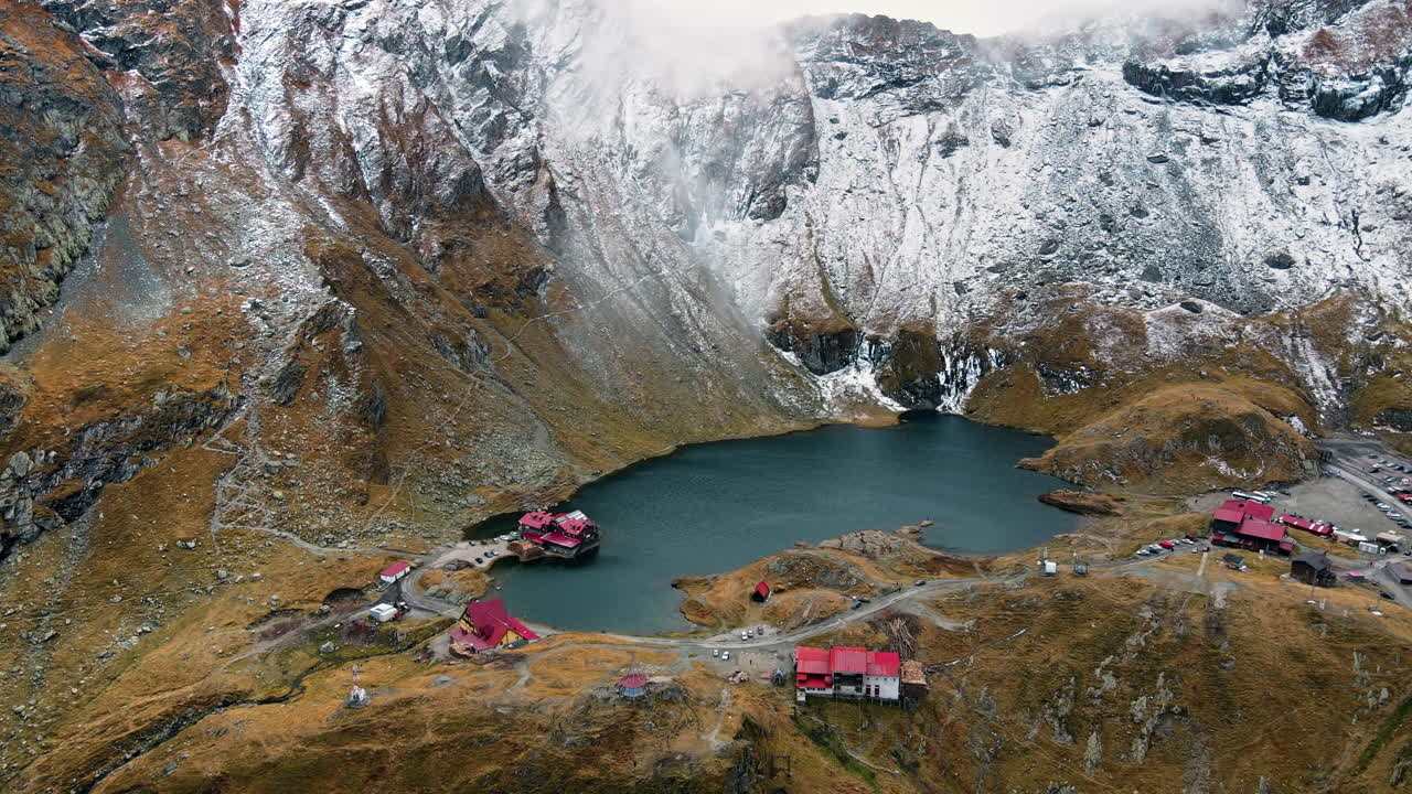 Aerial drone view of nature in Romania. Transfagarasan route in Carpathian mountains, Balea Lake resort and rocky slopes covered with snow, clouds