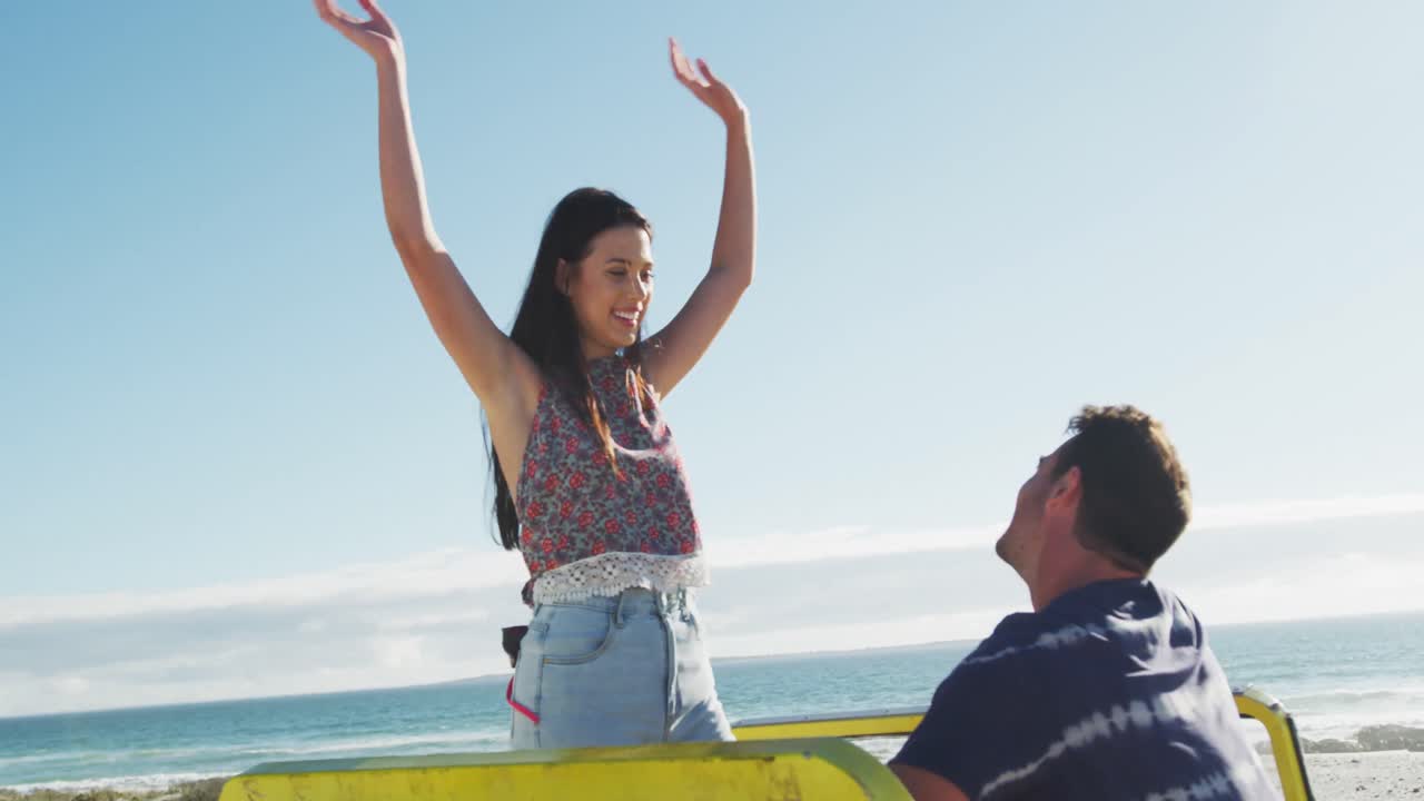 pareja caucásica sentada en un buggy de playa junto al mar hablando y bailando