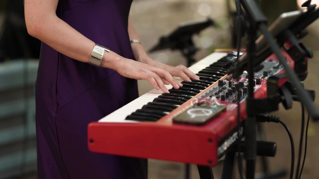 Mani del tastierista sui tasti rossi del pianoforte da palco con cavi e aste microfoniche a un evento dal vivo
