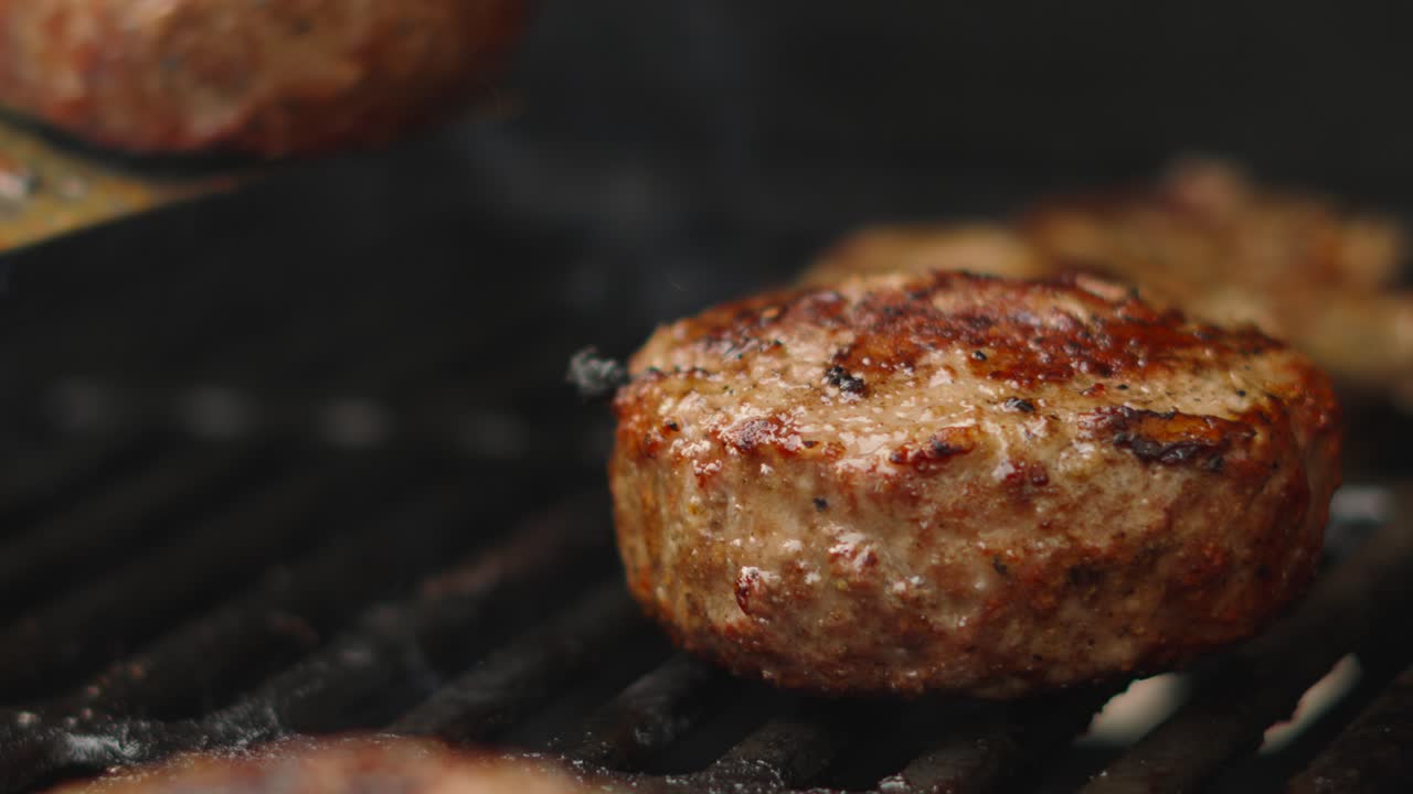 Close Up Details of Large Beef Patty Being Cooked on BBQ Grill with Juices Bubbling from Meat as it Cooks. Burger Flipped Over in Slow Motion