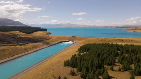 Drone-view-of-man-made-power-canal-in-between-golden-plains-and-pine-forests-at-Lake-Pukaki,-New-Zealand